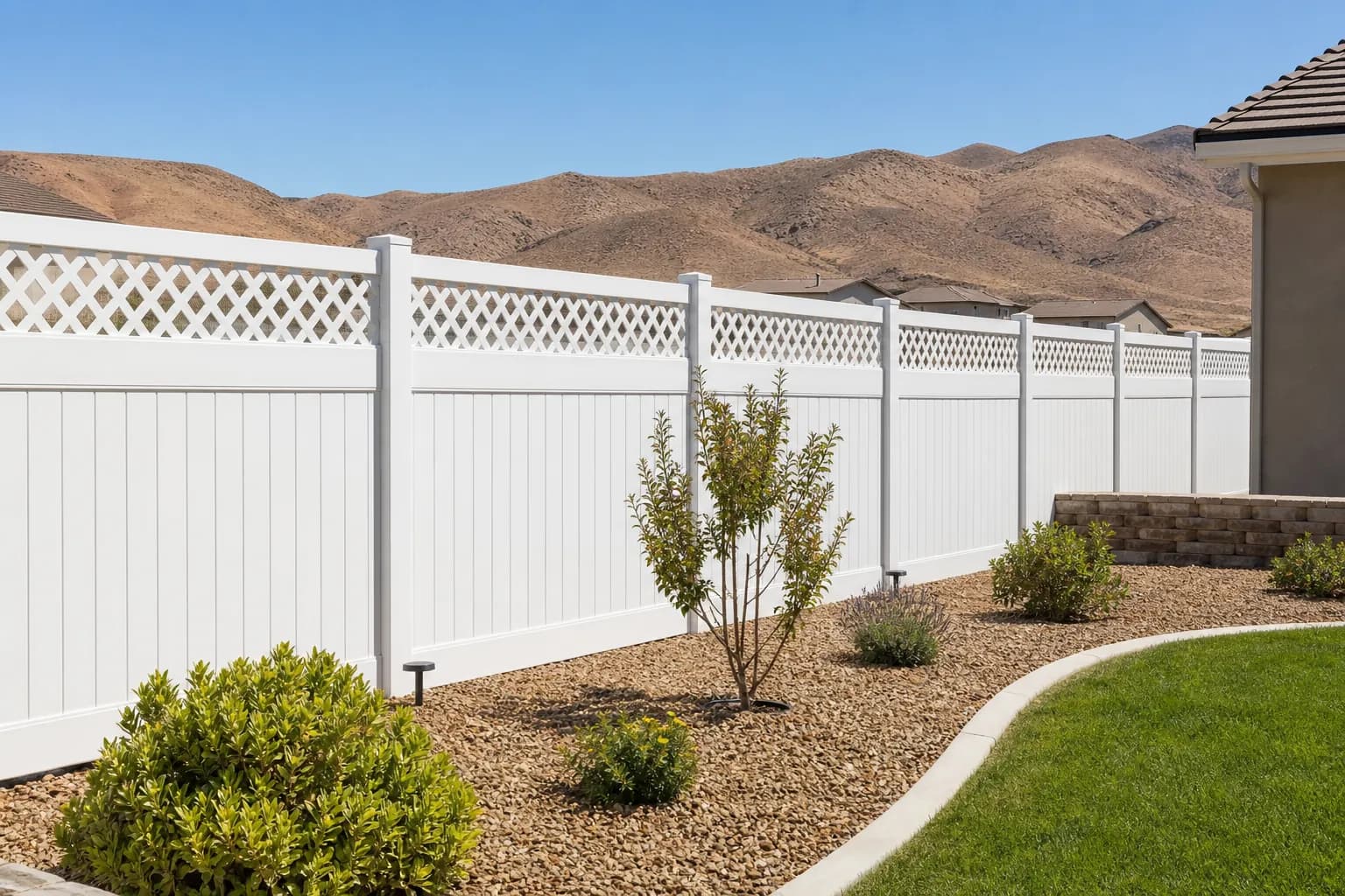 White vinyl privacy fence with a lattice top along a backyard in a newer subdivision with brown hills behind