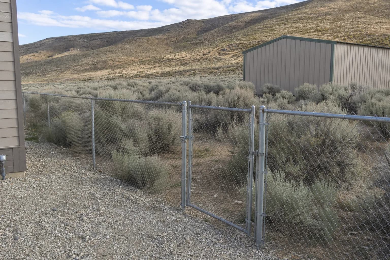 Galvanized chain link fence with a top rail and walk gate along a gravel side yard on a large rural lot