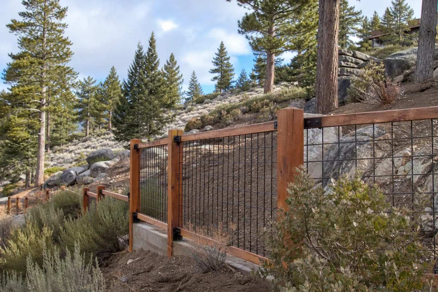 Cedar-framed welded wire fence stepping up a sloped lot among granite boulders and pines