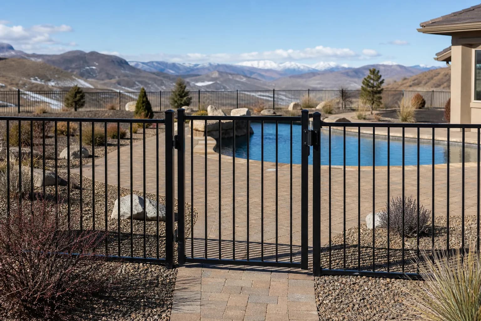 Black aluminum fence with a self-closing gate around a backyard pool with pavers and desert plants