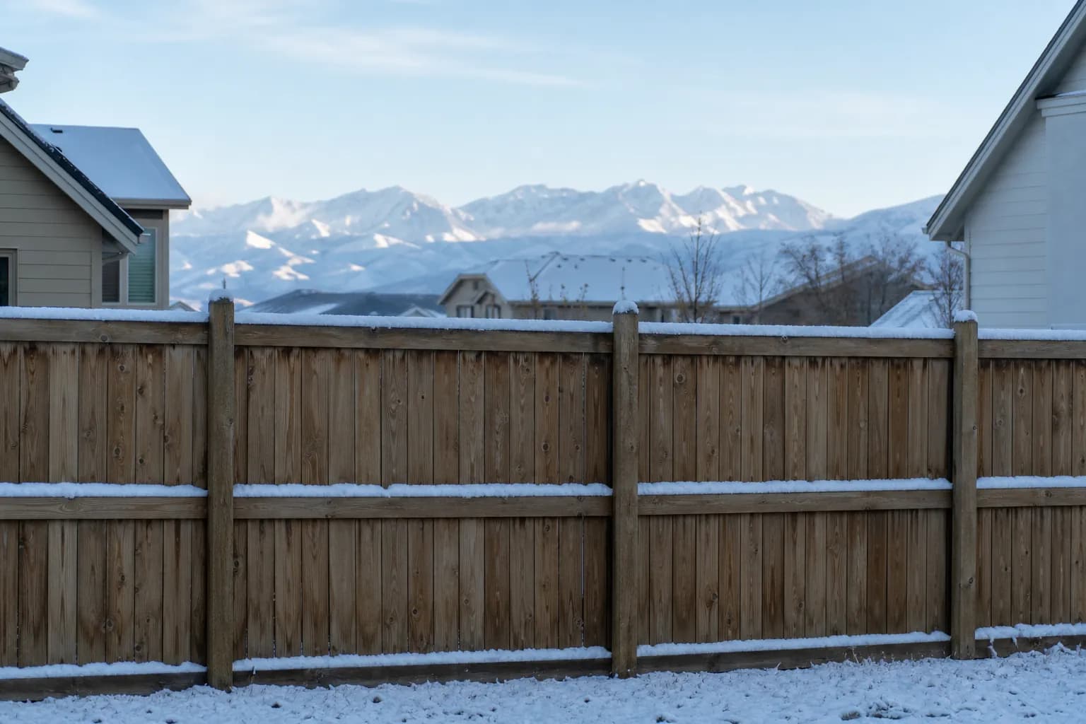Wood privacy fence in a Reno subdivision after a light snow, with the Sierra in the distance